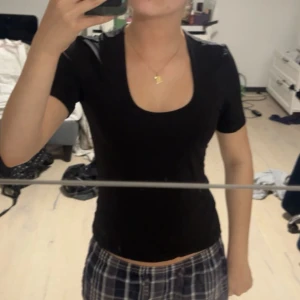 Svart topp från Comma - En svart, tight topp från Comma med korta ärmar och djup rundringning. Enkel och stilren design som passar till många olika outfits. Storlek 36.