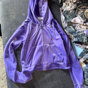 Lila velour hoodie från Juicy Couture & byxa med fjäril  - Lila hoodie i mjuk velour från Juicy Couture med dragkedja och huva. Broderad fjäril och logga på ryggen samt liten logga framtill. Perfekt för en avslappnad och trendig look. Byxor är också med för ett komplett sett! Storlek L i koftan storlek M i byxan. Väldigt unik modell som få personer har i sin garderob!