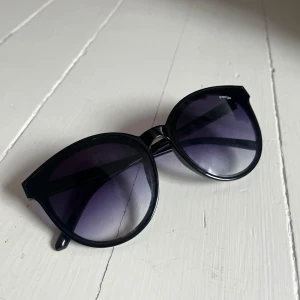 Svarta solglasögon med rundade bågar - Stilrena svarta solglasögon från Prestige med stora, rundade bågar och mörka glas. Perfekta för att ge en cool look och skydda ögonen mot solen. Passar dig som gillar klassisk och trendig stil.