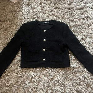 Svart cardigan jacka - Stilren svart jacka från gina tricot med rund halsringning och fyra dekorativa silverfärgade knappar framtill. Jackan har två fickor framtill och är tillverkad i ett strukturerat tyg som ger en exklusiv känsla. Tyget på högra armen är tovig men annars perfekt att slänga över en topp för en snygg look.