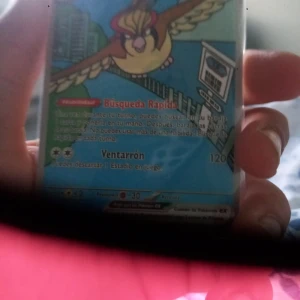 Pokémonkort Pidgeot EX på spanska - Säljer ett Pokémonkort med Pidgeot EX, text på spanska. Kortet har färgerna blå, gul och röd med illustration av Pidgeot som flyger. Energisymboler och attacknamn syns tydligt. Perfekt för samlare eller Pokémonfans.