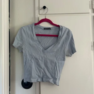 Ljusblå topp från Brandy Melville - Ljusblå lätt croppad t-shirt från Brandy Melville med v-ringning och korta ärmar. Tunt, ribbat material och diskreta ränder. Perfekt för en avslappnad stil. Superfin färg till våren och sommaren🥰 onesize men passar XXS-liten M.