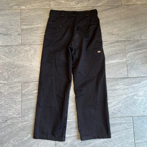 Svarta arbetsbyxor från Dickies - Svarta byxor från Dickies med raka ben och klassisk arbetsbyxstil. Byxorna har fickor bak och på sidan samt Dickies-logga på benet. Perfekta för en avslappnad och stilren look.