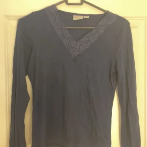 Blå långärmad topp med spets - Säljer en blå långärmad topp med v-ringning och dekorativ spets runt halsen. Perfekt för dig som gillar enkla men fina detaljer. Skön och mjuk känsla, passar till många olika outfits.