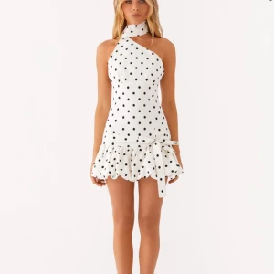 Vit prickig kortklänning med volang och rosett - INTRESSEKOLL!!! Superfin vit kortklänning med svarta prickar och unik one shoulder-design. Klänningen har volang nertill, stor rosett i midjan och en bred halsringning som går upp runt halsen. Perfekt för dig som vill sticka ut 