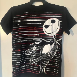 Svart t-shirt med Jack Skellington-tryck XS - Cool svart t-shirt med stort tryck av Jack Skellington från The Nightmare Before Christmas. T-shirten har vita och röda linjer samt korta ärmar. Perfekt för dig som gillar film och unika motiv. Helt ny. XS.