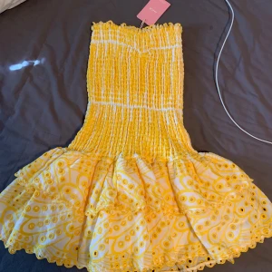 Gul sommarklänning - Solina från Design by Amor - Supersöt gul klänning med smockad överdel och voluminös kjol med broderade detaljer. Klänningen är ärmlös och har ett lekfullt mönster i gult och vitt. Perfekt för somriga dagar när du vill sticka ut lite extra. Nypris 549kr