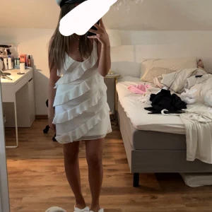 Student klänning  - Säljer en söt vit klänning med smala axelband och flera lager volanger. Klänningen har en kort, figurnära passform och är perfekt för sommarens tillfällen eller studentfirande. Enkel och stilren design som känns både trendig och fräsch. Har sytt om den i ryggen men inget som syns. Köpt för 600. 