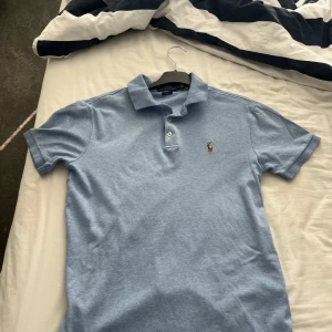 Ljusblå pikétröja från Polo Ralph Lauren - Säljer en ljusblå pikétröja från Polo Ralph Lauren i slim fit-modell. Tröjan har klassisk krage, knappar framtill och den. Storlek M men den är liten o storleken passar S bättre 