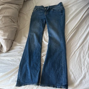 Blå bootcut jeans från Levis - Säljer ett par klassiska blå bootcut jeans från Levis med fem fickor och dragkedja. Jeansen har en något utsvängd passform nertill och är tillverkade i jeansmaterial. Perfekta för dig som gillar en retrostil. Som du kan se har den typ två hål där bak ( men det är väl inget man kan fixa) 