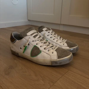 Philippe Model vita och grå sneakers med gröna detaljer - Snygga sneakers från Philippe Model i vitt och grått med gröna detaljer. Skorna har snörning, rund tå och platt sula. Märkeslogga på hälen och ovansidan, samt kontrastpaneler i mocka och skinn. Storlek 41! Skon i säg är i bra skick lite små skavanker. Sulan är även i fint skick. Skriv gärna om du har någon fråga 💬 Kom gärna med pris förslag! 