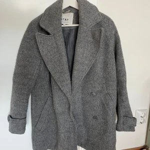 Grå kappa från Stay - Säljer en klassisk grå kappa från Stay med bred krage och dubbelknäppning. Kappan är varm, är i storlek S och är i bra skick, är lite nopprig från användning men ingen mer märkbart slitage.