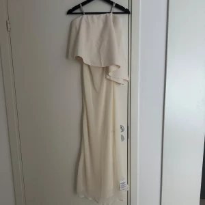 Vit långklänning med volang från ASOS DESIGN - Elegant vit långklänning från ASOS DESIGN med asymmetrisk volangdetalj upptill och axelbandslös design. Prislapp kvar.