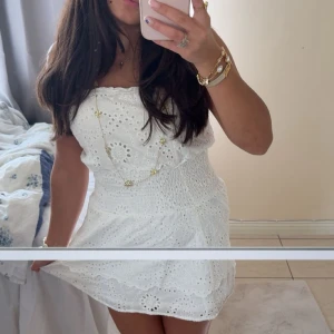 Vit axelbandslös klänning med broderade detaljer - Söt vit off shoulder klänning med broderade blommönster och smockad midja. Klänningen har en kort längd och är perfekt för varma dagar. Lätt och luftig känsla med fina detaljer som är perfekt för strand dagar. Köpt i en liten lokal butik i USA! Skriv vid funderingar!💓😚