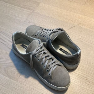 Grå mockasneakers från Sneaky Steve - Säljer ett par stilrena grå sneakers från Sneaky Steve i mocka. Skorna har snörning och en platt vit sula. Perfekta för dig som gillar en enkel och klassisk look till vardags.