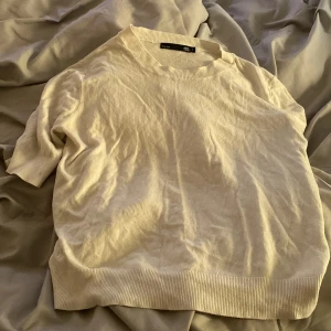 Vit kortärmad tröja  - Säljer en stilren vit kortärmad tröja. Tröjan har rund halsringning och breda ribbade muddar vid ärmslut och nederkant. Perfekt för en enkel och clean look.