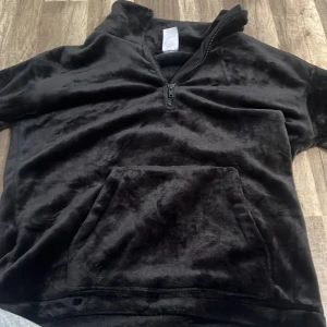 Svart fleece hoodie från Kappahl - Mysig svart hoodie i mjuk fleece från Kappahl. Tröjan har halv dragkedja framtill, stor känguruficka och långa ärmar. Perfekt för kalla dagar när du vill vara extra bekväm.