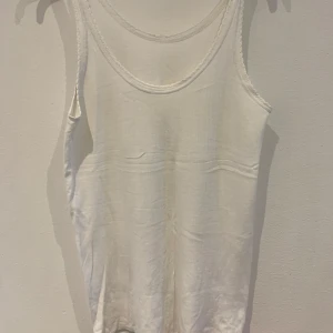 Vit ribbad linnetopp med spetskant - Säljer en enkel och stilren vit linnetopp med ribbad struktur och fina spetsdetaljer längs kanterna. Perfekt att matcha med jeans eller kjol för en fräsch look.