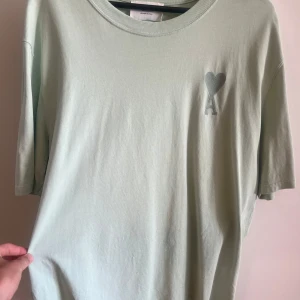 Mintgrön t-shirt från Ami Alexandre Mattiussi - Säljer en mintgrön t-shirt från Ami Alexandre Mattiussi med ett broderat hjärta och A på bröstet. T-shirten har rund halsringning och är kortärmad. Köpt i Amis affär i New York, sparsamt använd