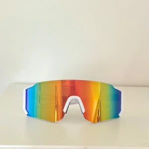 Tuffa sportiga solglasögon  - Säljer ett par sportiga solglasögon med vita bågar och stora, regnbågsfärgade spegelglas. Glasögonen har en modern, kantig form och passar perfekt för träning utomhus☀️ Snygg och futuristisk look🔥