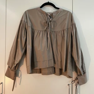 Brun-beige blus - Säljer en helt ny brun-beige blus från Gina Tricot med volangdetaljer, ballongärm samt knytdetaljer. Färgen är lite ljusare i verkligheten än i bilden. Har aldrig används bara hängt inne i garderoben. Storleken är 32, men skulle passa lika bra för dig som har 34-36. Priset kan diskuteras. 