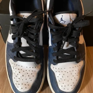 Jordan 1 Retro Low Golf Midnight Navy - Säljer ett par Nike Air Jordan 1 Low OG i navy och vitt. Skorna har klassisk svart swoosh, perforerad tå och svart snörning. Yttermaterial i skinn och sula i gummi. Perfekta för dig som gillar streetwear och sneakers med ikonisk design. Observera skicket på bilderna!