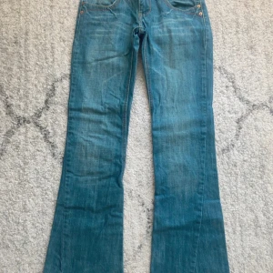 Blå bootcut jeans från Dolce & Gabbana - Vintage Low bootcut jeans Dolce Gabbana med röd och gul söm med en stor logga vid fickorna.  Innerbenet: 75cm Midja: 34cm. Jeansen har låg midja, fem fickor och slitna detaljer vid bensluten. Perfekta för dig som gillar en retro vibe och vill ha ett par jeans med snygg passform. 