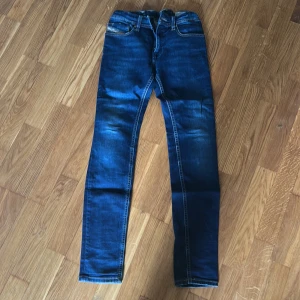 Blå Diesel Sleenker J-N jeans slim-skinny - Säljer ett par blå jeans från Diesel, modell Sleenker J-N. Jeansen har slim-skinny passform, klassisk femficksdesign och snygga slitningar framtill. Stretchigt material för extra komfort. Perfekta för dig som gillar smalare jeans med modern look.