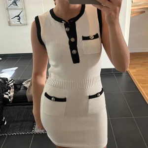 Vit stickad ärmlös klänning med svarta detaljer - Supersnygg vit stickad klänning med svarta kanter och silverfärgade knappar. Ärmlös modell med tight passform!