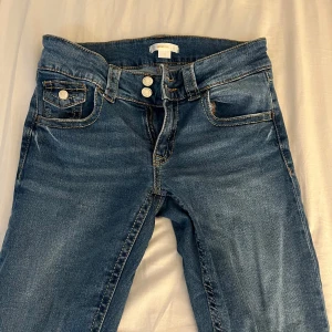 Blå jeansbyxor från Gina Tricot - Säljer ett par klassiska blå jeans från Gina Tricot med normal passform. Byxorna har fem fickor, dubbla knappar och dragkedja framtill. Snygga kontrastsömmar och raka ben. Perfekta till vardagslooken.