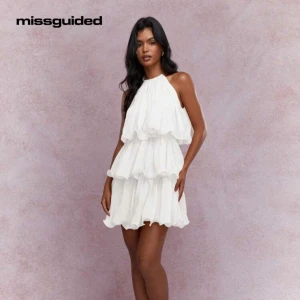 Vit volangklänning/Studentklänning från Missguided - Supersöt vit klänning med flera lager volanger och halterneck. Kort modell med luftig passform. Klänningen har en ärmlös design och lätt, flowigt material. Jag säljer klänning eftersom den var för genomskinlig för mig och har köpt en annan studentklänning. Endast testad!