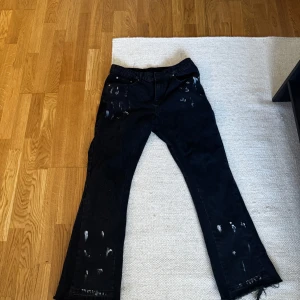 Flared jeans med färgstänk - Svarta jeansbyxor med raka ben och unika vita färgstänk över hela byxorna. Klassisk femficksmodell med knapp och dragkedja i midjan. Perfekta för dig som vill sticka ut med en kreativ och edgy stil.