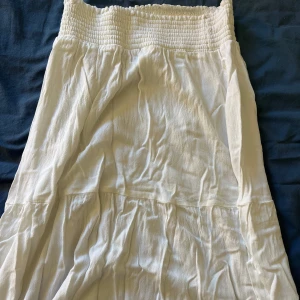 Vit långkjol - Säljer en vit långkjol med smockad midja och lätt, luftig känsla. Kjolen har en enkel design och är perfekt för varma dagar. Passar dig som gillar en avslappnad och somrig stil.