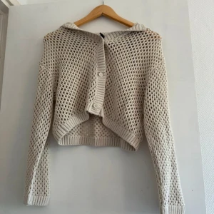 Beige stickad kofta från Divided XS - Snygg beige stickad kofta från Divided i öppen mesh-look. Croppad modell med lång ärm, ribbade muddar och knappar framtill. Perfekt för lager-på-lager och chill vårstil.