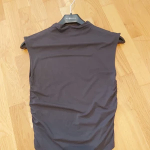 Mörkgrå ärmlös topp - Snygg mörkgrå ärmlös topp med enkel och stilren design. Toppen har en rak passform och är tillverkad i ett mjukt och stretchigt material som känns skönt mot huden. Perfekt att matcha med jeans eller kjol för en clean look.