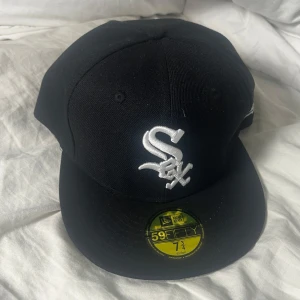 Svart New Era 59FIFTY White Sox keps - Snygg svart keps från New Era 59FIFTY med broderad vit White Sox-logga framtill. Klassisk rak skärm och Cooperstown Collection-märke på insidan. Perfekt för dig som gillar sportig streetstyle och vill ha en ikonisk look.