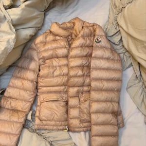 Rosa dunjacka från Moncler - Säljer min rosa/beiga dunjacka från moncler i storlek 1, den är väll använd med vissa fläckar såsom sminkfläckar   