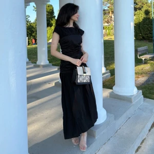 Svart långklänning med rynkade detaljer - Säljer en svart långklänning med snygga rynkade detaljer i midjan och överdelen. Klänningen har korta ärmar och en rak, elegant siluett. Perfekt för dig som gillar stilrena och tidlösa plagg. Materialet känns lätt och följsamt.