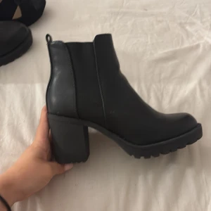 Svarta stövletter från Anna Field - Säljer ett par svarta stövletter från Anna Field i skinnimitation med chunky klack och grov sula. Skorna har elastiska paneler på sidorna för enkel påtagning och en klassisk rund tå. Perfekta till höst och vinter för en snygg och edgy look.