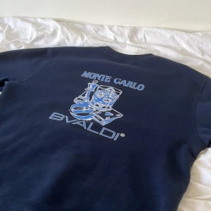 Mörkblå sweatshirt från Bvaldi  - Snygg mörkblå sweatshirt från Bvaldi med coolt Monte Carlo-tryck på ryggen och liten logga framtill. Klassisk rund hals och mjukt material som känns skönt mot huden. Perfekt för dig som gillar stilrena och sportiga vibes.