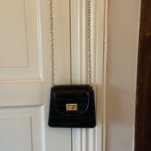 Liten svart väska med guldig kedja - Svart väska med guldig kedja. Väskan är väldigt liten.