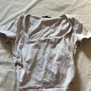 Vit topp med fyrkantig ringning från Zara - Säljer en stilren vit topp från Zara i storlek S. Toppen har en snygg fyrkantig ringning och korta ärmar. Tillverkad i mjuk bomull, perfekt att matcha med jeans eller kjol för en clean look.