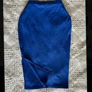 Kornblå tight långkjol med slits - Snygg kornblå långkjol i stretchigt material med tight passform. Kjolen har en liten slits på sidan och bred resår i midjan för extra komfort. En liten defekt på framsidan där en liten rapning har skett. Se sista bild 