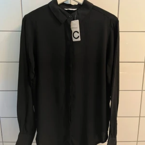 Svart skjortblus från Cubus - Stilren svart skjorta/blus från Cubus med klassisk krage och dolda knappar framtill. Oanvänd med lapp kvar