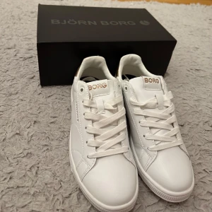 Vita skor från Björn Borg - Stilrena vita sneakers från Björn Borg med detaljer i guld på häl och logga. Skorna har aldrig används men säljer de eftersom när jag testade de var de för små, nypriset på de är ca 699, och de är väldigt fina, och såklart i väldigt fint skick, priset kan prutas i snabbaffär!