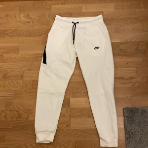 Vita mjukisbyxor från Nike - Säljer ett par vita mjukisbyxor från Nike med svart logga på låret och svarta snören i midjan. Byxorna har slim passform, muddar vid bensluten och är tillverkade i mjukt material. Perfekta för chill eller träning. Ny köpta, fick dem i present och aldrig använt dem själv. Jag är 180 cm.