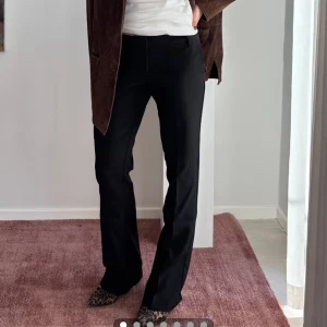 Bikbok Svarta kostymbyxor med bootcut - Snygga svarta kostymbyxor med bootcut-silhuett och klassisk passform. Byxorna har medelhög midja och raka ben som får en lätt utsvängd look nertill. Perfekta till både sneakers och klackar. Stilrena och enkla att matcha med olika outfits.