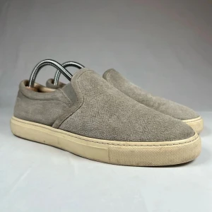 BRUNELLO CUCINELLI skor  - Stilrena slip-on sneakers i beige mocka med platt sula och rund tå. Skorna har elastiska paneler på sidorna för enkel påtagning och en krämfärgad yttersula som ger en clean look. Perfekta för dig som gillar minimalistisk och avslappnad stil.