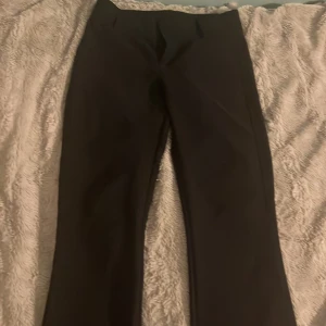Svarta kostymbyxor från Gina Tricot - Säljer ett par svarta kostymbyxor från Gina Tricot i storlek M. Byxorna har raka ben, hög midja och snygga bakfickor med knappar. Perfekta för en clean och stilren look. Materialet känns mjukt och följsamt.