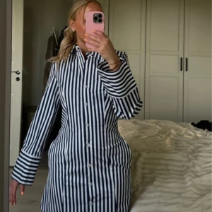 Randig skjortklänning från COS - Snygg skjortklänning från COS i vita och marinblåa ränder. Klänningen har lång ärm, knappar hela vägen framtill och klassisk krage. Figursydd modell som går in vid midjan och som har fickor i sidorna 🫶🏽